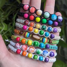 a hand is holding several bracelets with different colored beads on them and one has a green leaf in the background