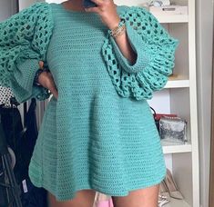 a woman taking a selfie in front of a mirror wearing a blue sweater with crocheted sleeves