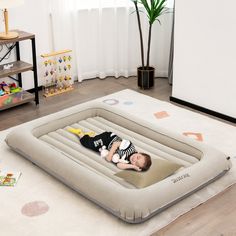 a baby laying in an inflatable bed on top of a floor next to a potted plant