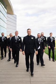 a group of men in tuxedos walking down a sidewalk