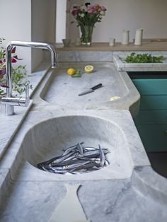 a sink in a kitchen with lots of clutter on the counter and flowers behind it