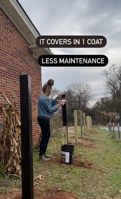 a woman standing in front of a brick building holding a black pole with the words, it covers in 1 coat less maintenance