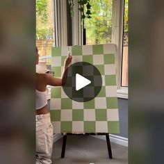 a woman standing in front of a green and white checkerboard easel holding a piece of art