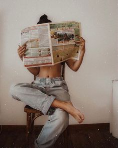 a woman is sitting on a chair and reading a newspaper with her hands behind her head