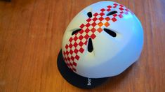 a helmet with red and white checkered design on the side sitting on a wooden surface