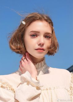 a woman with short hair wearing a white blouse and holding her hand on her shoulder