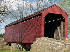 a red covered bridge in the middle of a grassy area with trees and rocks around it