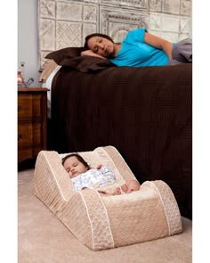 a woman laying on top of a bed next to a baby in a crib