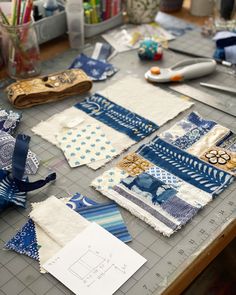 many pieces of fabric are laid out on a table with scissors and sewing supplies in the background