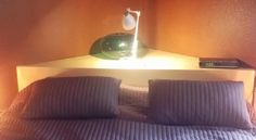 a bed with two pillows and a lamp on top of it in a room that has orange walls