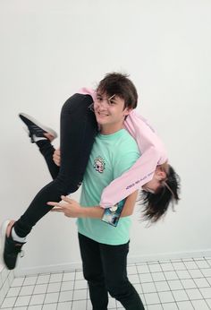 two people standing in a room one holding the other upside down and smiling at the camera