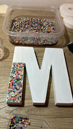 the letter m is made out of beads and plastic wrappers next to a container of candy