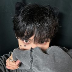 a man with black hair and piercings covering his face behind a gray hoodie