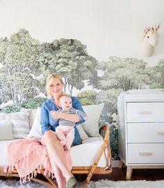 a woman holding a baby in her arms while sitting on a couch next to a wall mural