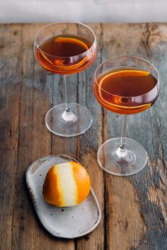 two glasses of wine and an orange peel on a wooden table with one glass filled with liquid