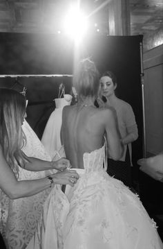 a woman in a wedding dress is helping another woman get ready for her big day