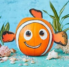 an orange clown fish pumpkin sitting on top of a blue table next to sea shells