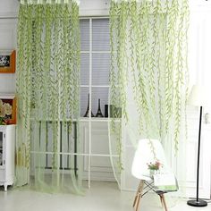 a living room with white walls and green curtains on the windowsill, along with a chair