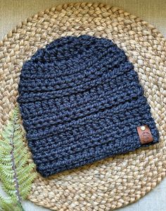 a blue crocheted hat sitting on top of a woven place mat next to a plant