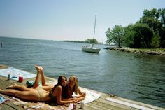 two women are laying on a dock by the water