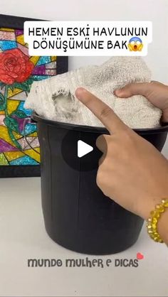 a person pointing at a trash can with a towel in it and another hand touching the lid