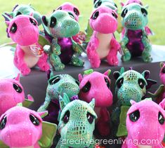 several pink and green dragon stuffed animals sitting on top of a black table with grass in the background