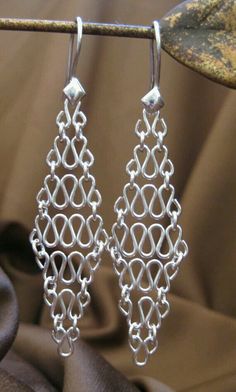 two pairs of silver earrings are hanging from a metal hook on a piece of fabric