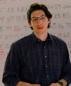 a man standing in front of a whiteboard with numbers on it and writing on the wall behind him