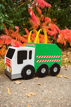 a green and white toy truck sitting on top of a gravel road next to trees