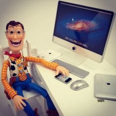 a toy man sitting at a computer desk with a cell phone in front of him