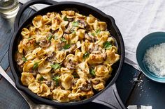 a skillet filled with pasta, mushrooms and parmesan cheese next to a bowl of seasoning