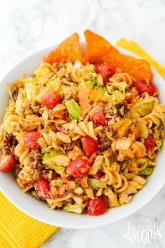 a white bowl filled with pasta salad next to tortilla chips on a yellow napkin