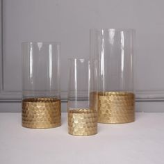 three gold colored glass vases sitting on top of a white table next to each other