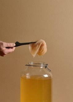 a person is holding a spoon over a jar with liquid in it and there is a piece of bread sticking out of the top