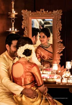 a man and woman sitting in front of a mirror with candles on the table behind them