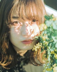 a woman with long hair holding flowers in front of her face and looking at the camera