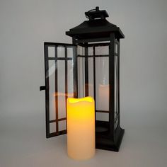 two lit candles sitting next to each other in front of a black lantern on a white background