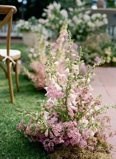 pink and white flowers in the grass next to a chair