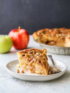 a slice of apple pie on a white plate with an apple in the back ground