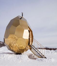 a large golden object sitting on top of snow covered ground next to a stair case