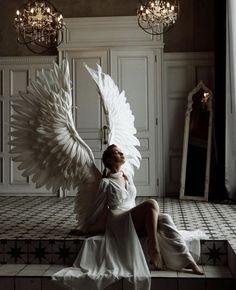 a woman sitting on top of a tiled floor next to a white angel wings statue