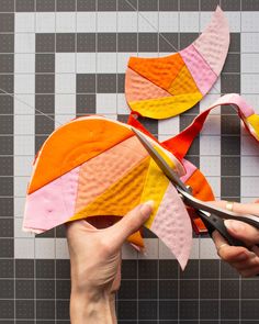 someone is cutting fabric with scissors on the table next to some pieces of paper that have been cut into shapes