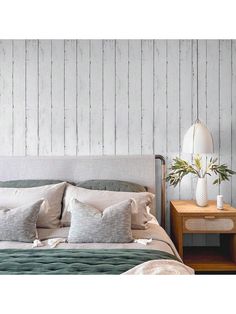 a bed with pillows and blankets in front of a white wooden headboard on the wall