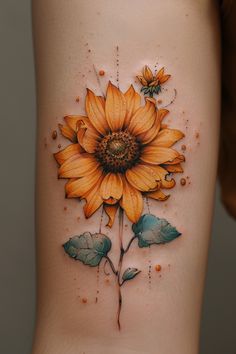 a yellow sunflower tattoo on the side of a woman's thigh, with leaves around it