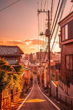 an empty street with power lines in the distance and buildings on both sides at sunset