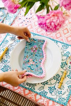 a person is setting a table with pink flowers and blue napkins on it,