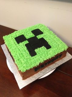 a cake with green frosting and black squares on it sitting on top of a wooden table