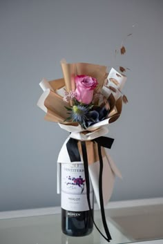 a wine bottle wrapped in brown paper with a pink rose