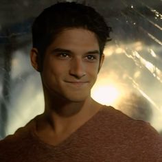 a close up of a person wearing a brown shirt and smiling at the camera with sunlight shining behind him