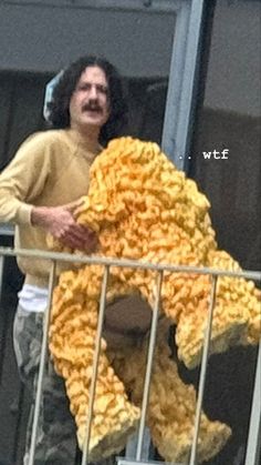 a man standing on top of a balcony next to a pile of yellow crochet